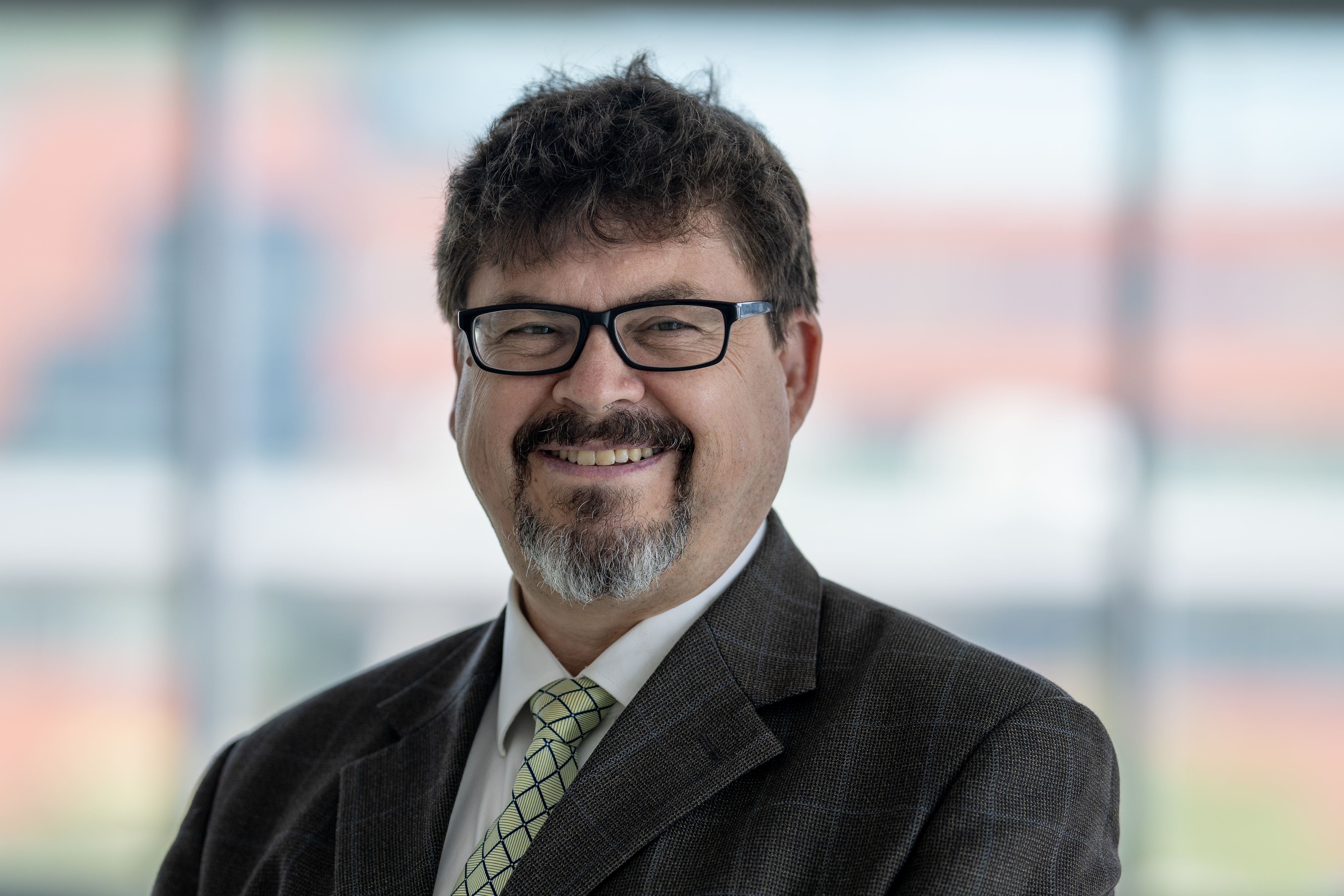 Man with dark hair and glasses wearing a tie and dark suit.